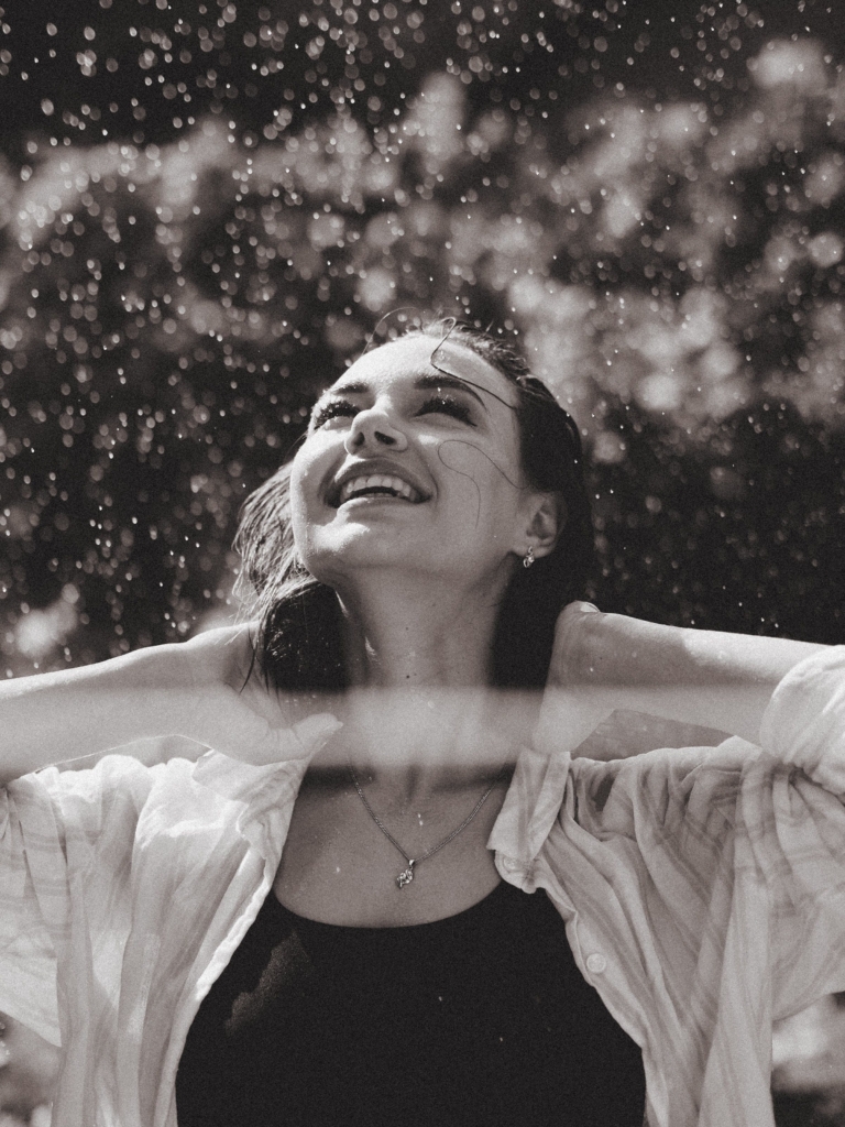 Smiling woman with wet hair enjoying rainfall outdoors